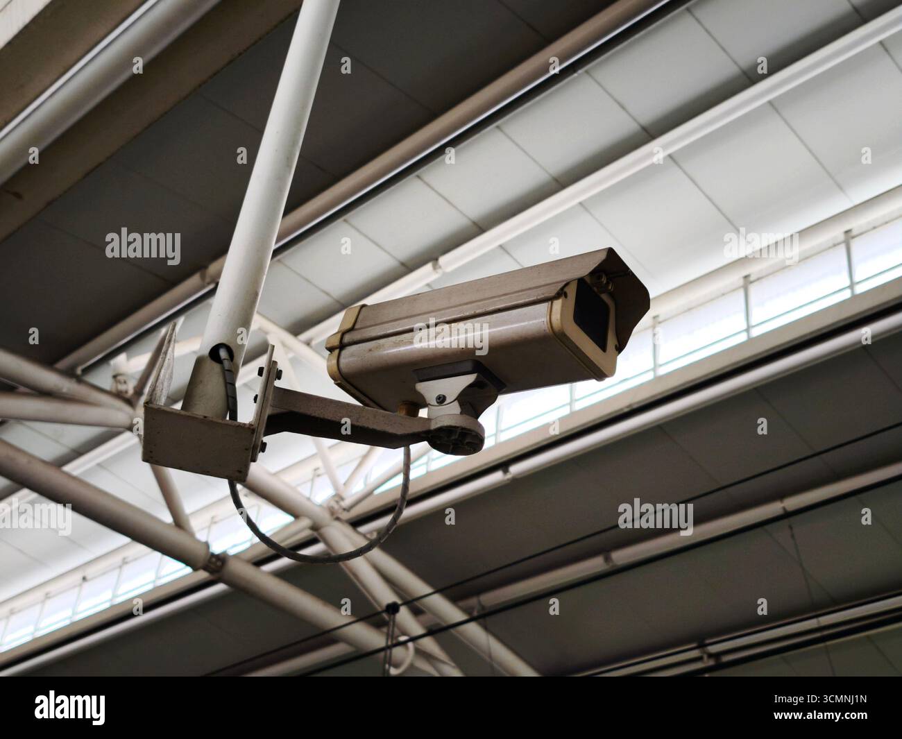 Eine Überwachungskamera auf einem Metallrahmen in einem Gebäude. Die Kamera befindet sich unter der Deckenkonstruktion. Stockfoto