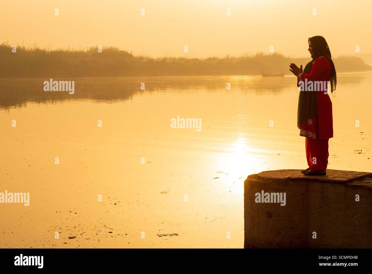 New Dehli, Indien - 30. März 2019 : Eine Frau betet am Fluss bei Sonnenaufgang, ihre Silhouette von goldenem Licht umrahmt, die Gelassenheit, Hingabe, Stockfoto