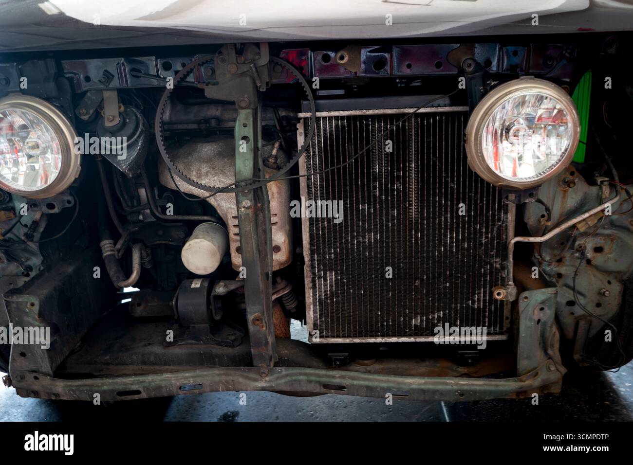 Vorderansicht eines Fahrzeugs in einer Werkstatt mit ausgebautem Stoßfänger und Kühlergrill, wobei zwei kreisförmige Scheinwerfer und ein Kühler freigelegt werden. Stockfoto