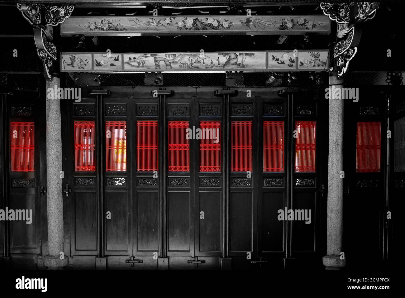 Traditionelle chinesische Architektur in selektiven Farben. Komplexe dunkle Schnitzereien stehen im Kontrast zu leuchtenden roten Fenstern, die eine dramatische, künstlerische Stimmung erzeugen. Stockfoto