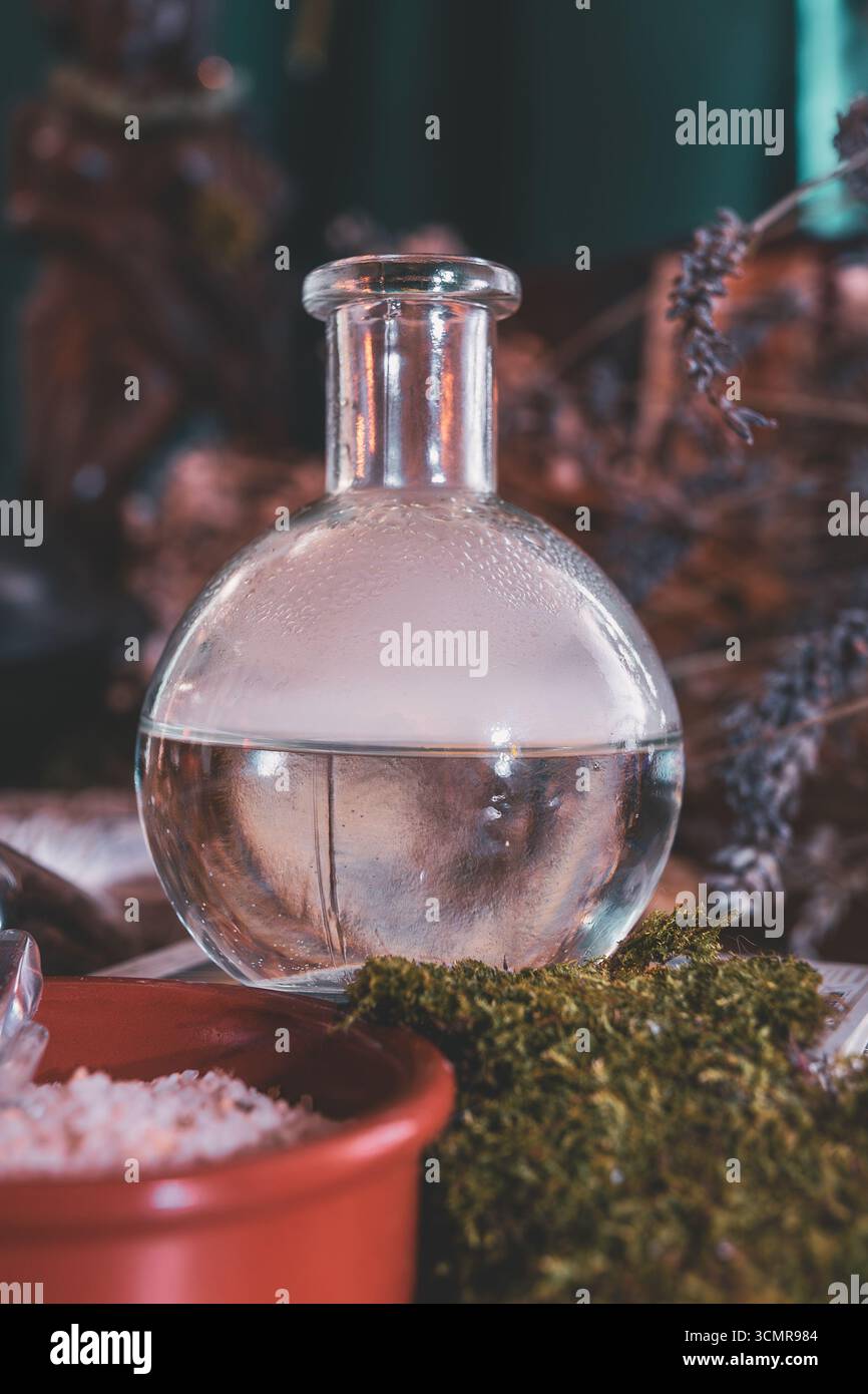 Nahaufnahme einer mystischen Tränkflasche umgeben von Moos, Kräutern und rituellem Salz auf einem spirituellen Wiccan-Altar. Stockfoto