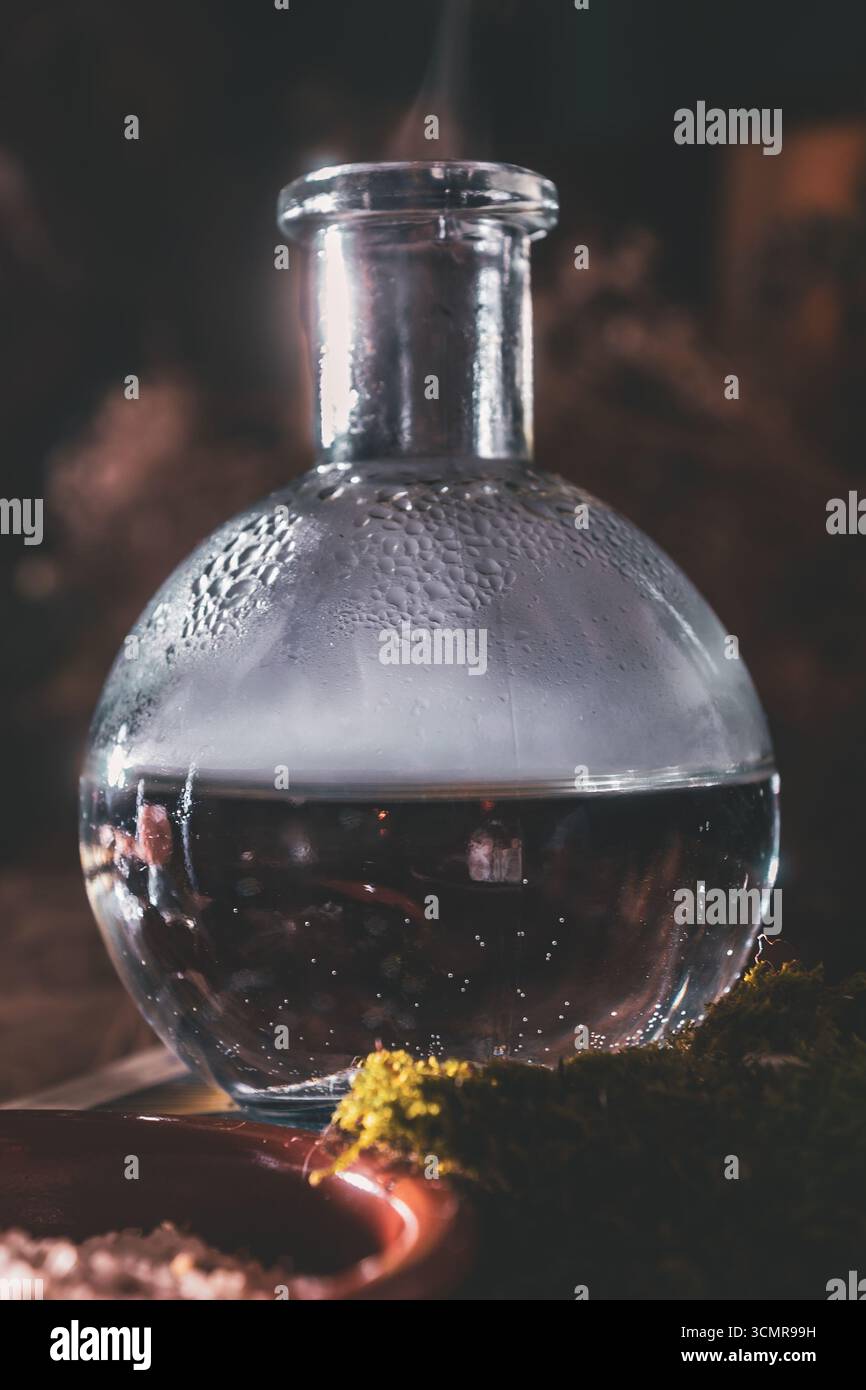Dampfende Glastränkflasche umgeben von Moos und Salz, Teil eines magischen Wiccan-Altars für rituelle und spirituelle Praktiken. Stockfoto