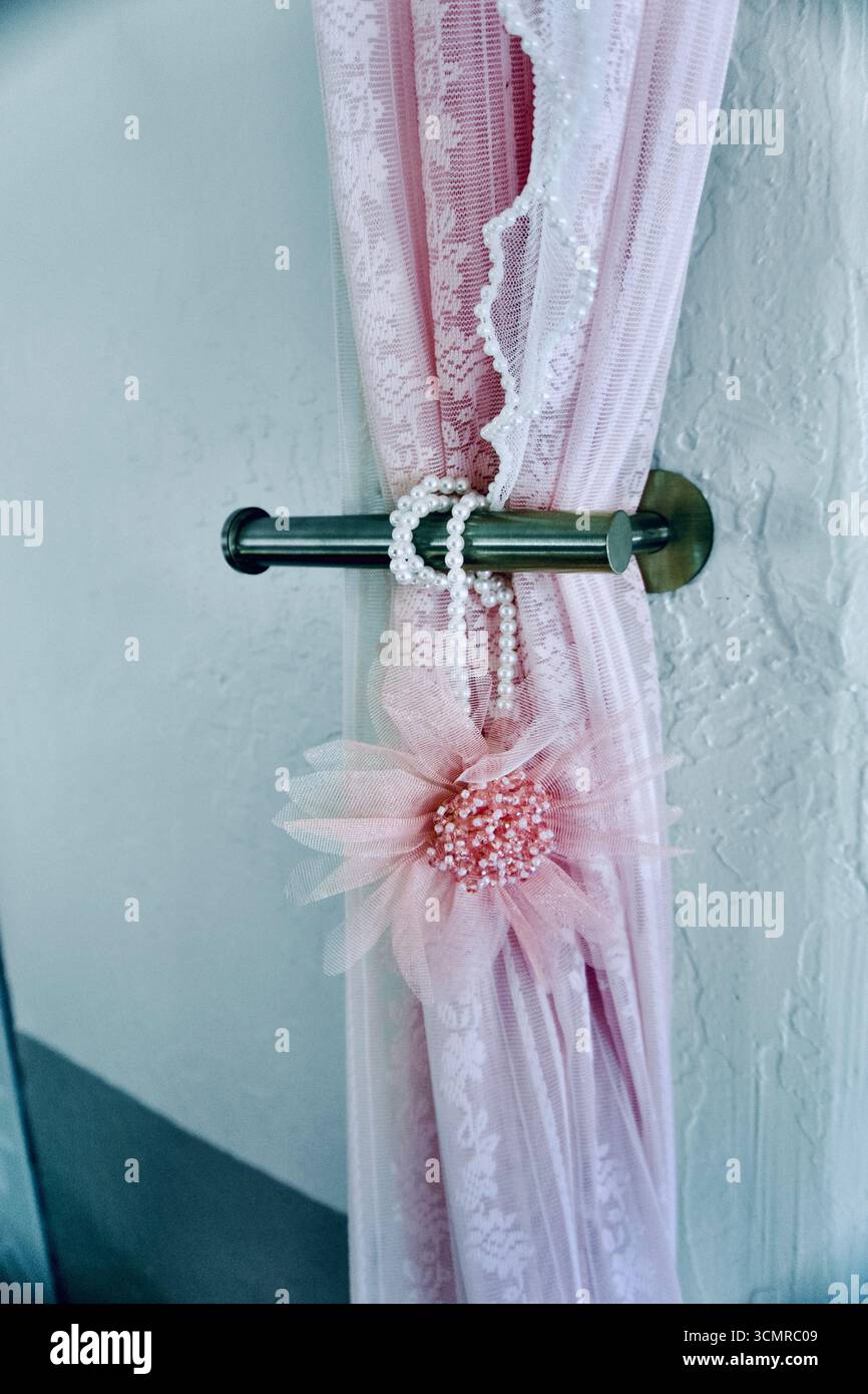 Pinkfarbener Spitzenvorhang mit Perlstickchen und perlenbesetzter Blume auf einem Metallstab Stockfoto