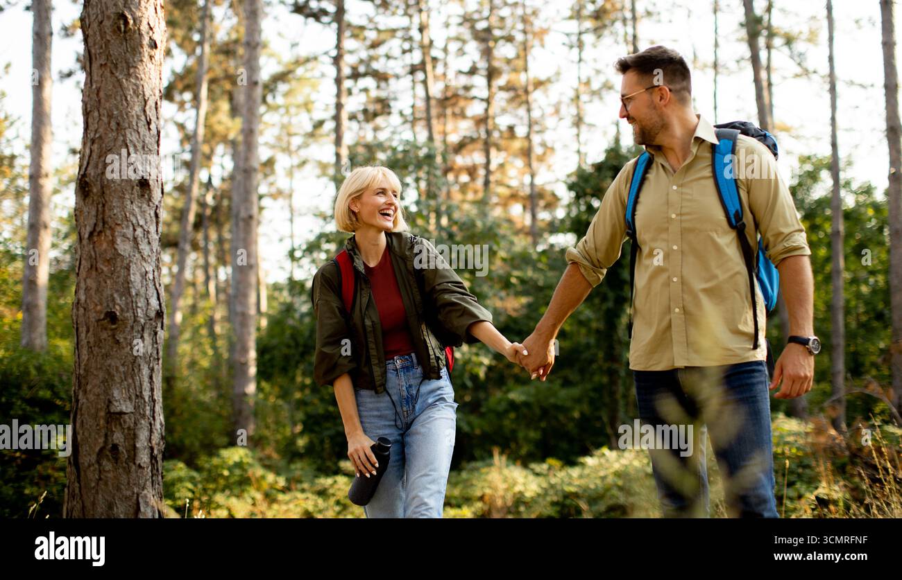 Ein Mann und eine Frau gehen Hand in Hand auf einem Waldweg entlang und genießen die Gesellschaft und die Schönheit der Natur an einem sonnigen Nachmittag. Lachen erfüllt Stockfoto