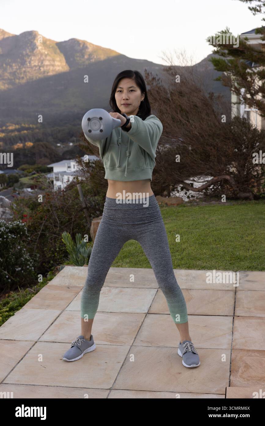 Asiatische Frau in Sportkleidung, die Krafttraining auf der Terrasse im Hinterhof durchführt Stockfoto