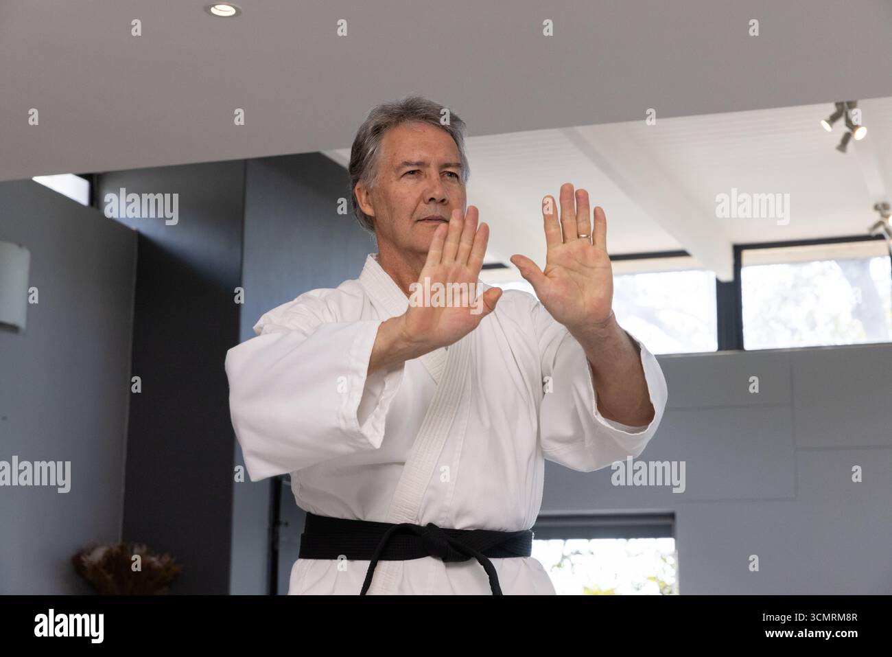 Senior-Mann mit Blockiertechnik im Kunststudio mit Karate-Gi und schwarzem Gürtel Stockfoto