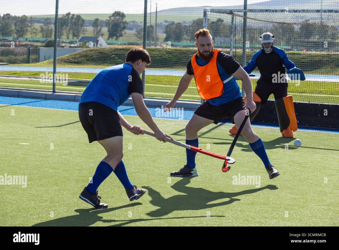 Männliche Athleten in Lätzchen und Torwartpads üben Hockeybohren auf Rasen mit Stöcken und Ball Stockfoto