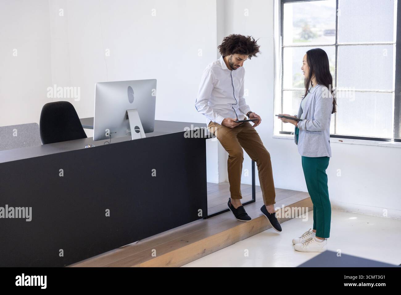 Verschiedene Kollegen stehen an der Rezeption im Büro mit Monitor, der Smartphone und Tablet hält Stockfoto