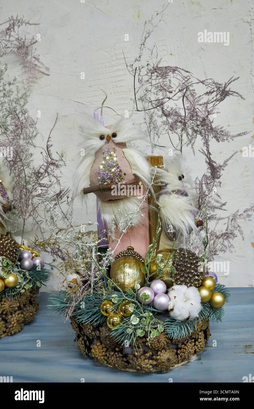 Elegantes, handgefertigtes Weihnachtszentrum mit lila Kerzen, Kiefernzweigen, goldenen und violetten Ornamenten, Baumwolle, Tannenzapfen und dekorativen Eulen. Perfec Stockfoto