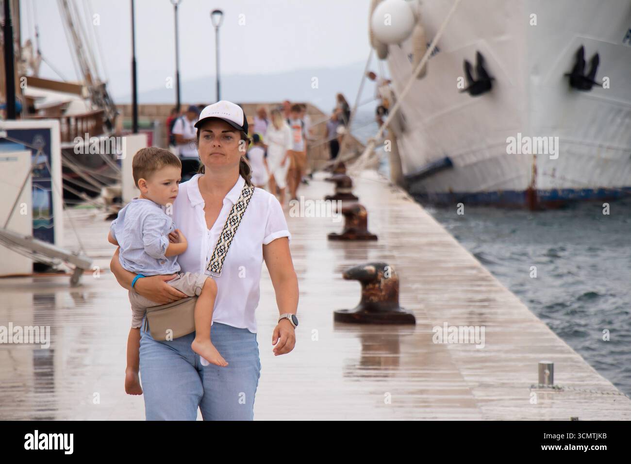 Vodice, Kroatien - 21. August 2025: Frau mit einem Jungen, der das Schiff im Hafengebiet verlässt, an einem nassen, bewölkten Sommertag an der kroatischen Küste Stockfoto