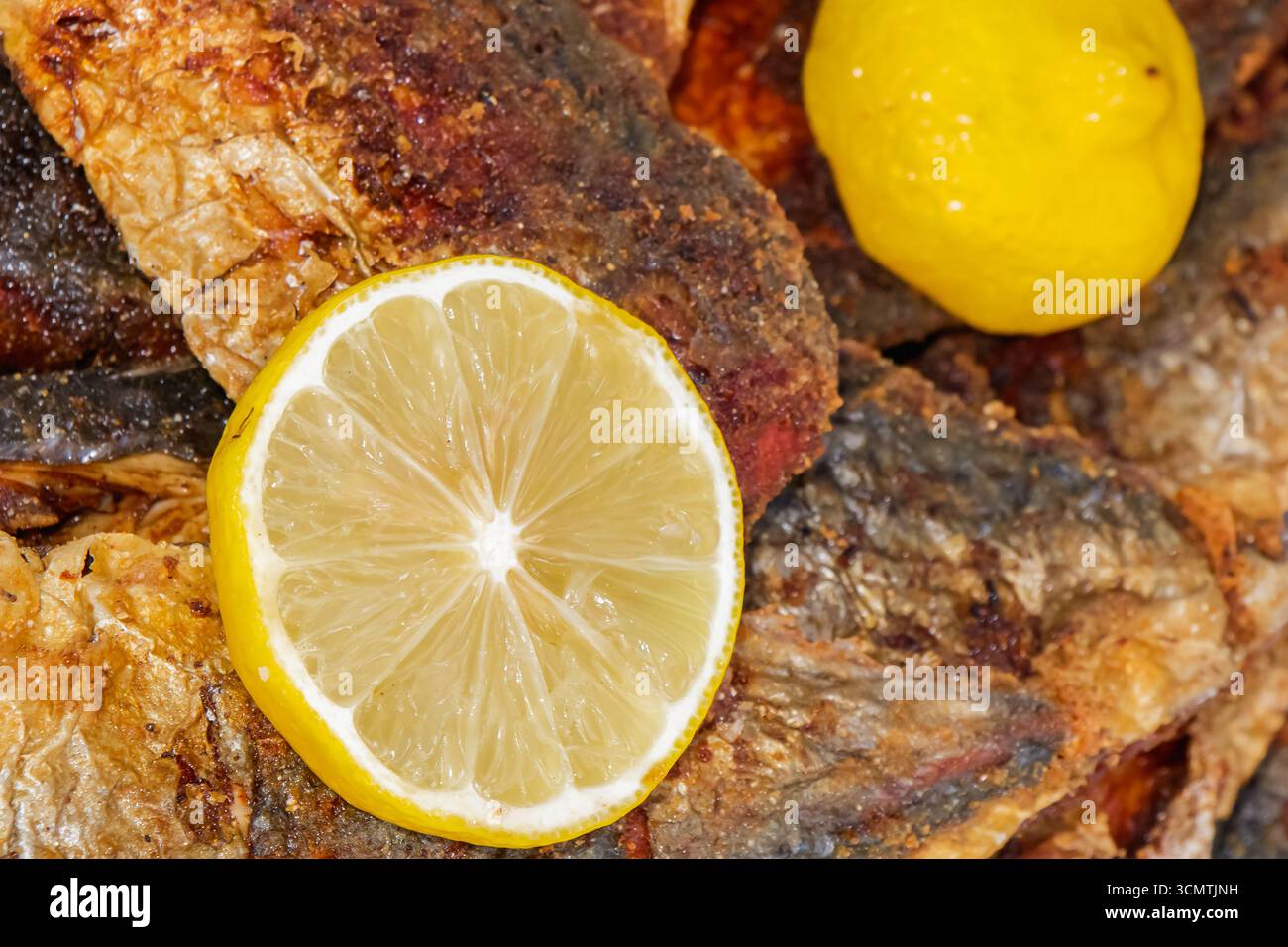 Nahaufnahme von gegrilltem Fisch mit goldknuspriger Haut, garniert mit Zitronenscheiben zur Garnierung, wodurch eine Präsentation mit frischen Meeresfrüchten entsteht, die für Menüs geeignet ist Stockfoto