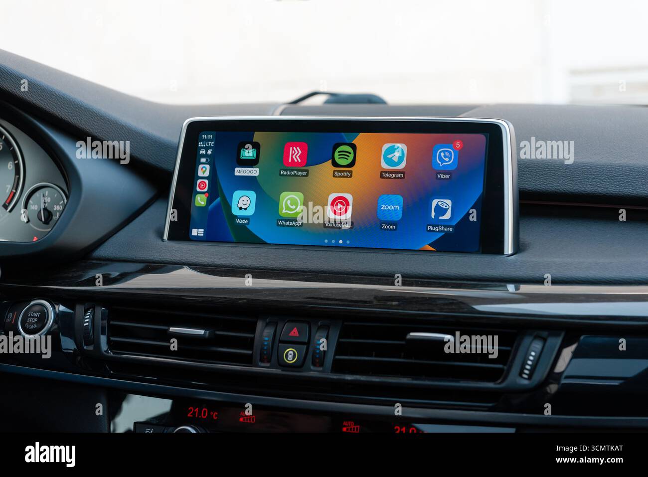 Apple CarPlay-Bildschirm mit Symbolen im modernen Auto. Fahrzeuginnenraum mit Hochglanzholz, Nahaufnahme des Infotainment-Systems. Stockfoto