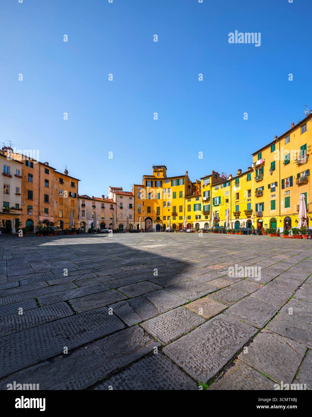 Mittelalterliche Piazza dell'Anfiteatro in Lucca mit farbenfrohen historischen Gebäuden, Steinpflaster und blauem Himmel. Berühmter ovaler Platz, der auf dem antiken Rom erbaut wurde Stockfoto