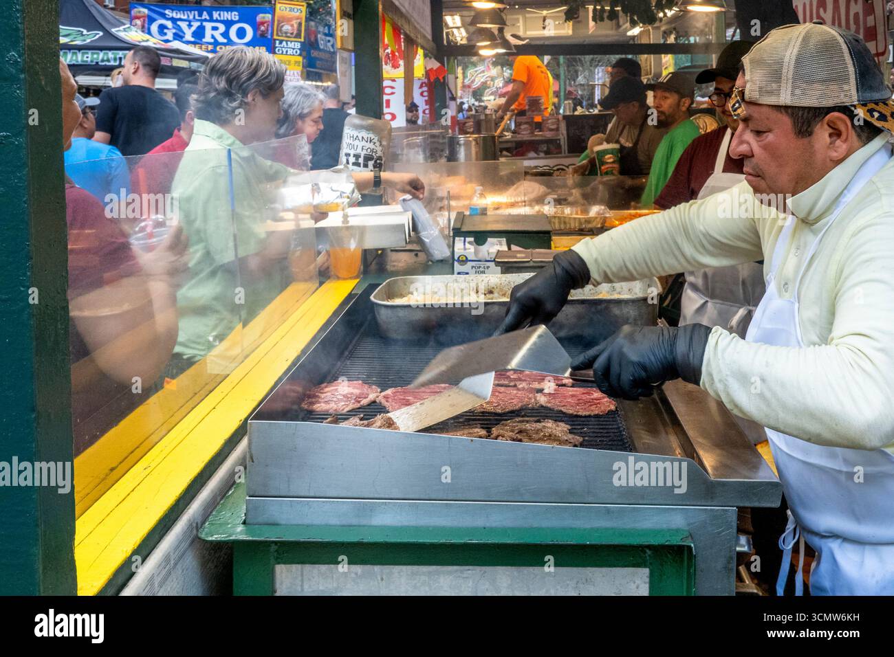 New York, NY - USA - 14. September 2025 Straßenverkäufer in Handschuhen und Schürzen grillt Rindfleisch-Steaks und Zwiebeln im Feast of San Gennaro, das Hungry fest serviert Stockfoto