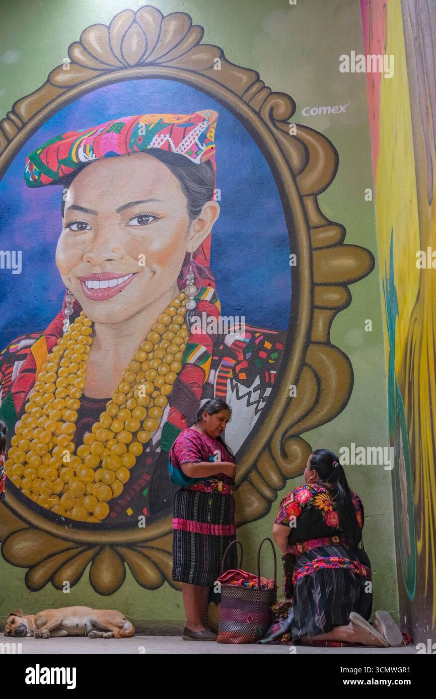 Chichicastenango, Guatemala - 3. Juli 2025: Frauen neben einem Wandgemälde des Künstlers Edwin Gonzalez auf dem Santo Tomas Markt in Chichicastenango, Guatemala. Stockfoto