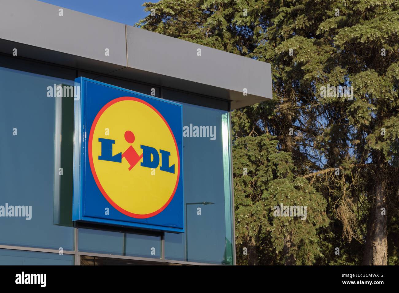 Das Lidl-Supermarktschild in Tomar, Portugal, ist auf einer modernen Glasfassade montiert. Das blau-gelbe Logo hebt sich vom Gebäude und der Umgebung ab Stockfoto