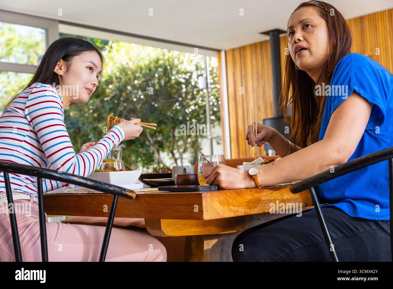 Asiatische Mutter und Tochter teilen sich das Abendessen an einem Holztisch zu Hause mit Essstäbchen Stockfoto