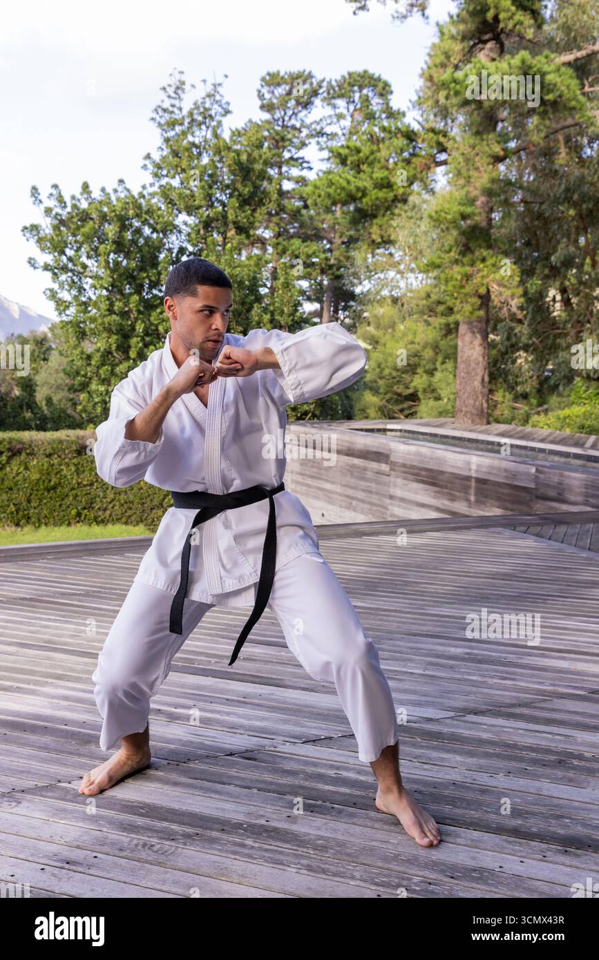 afroamerikaner üben Karate in weißem Gi und schwarzem Gürtel auf Holzplattform Stockfoto