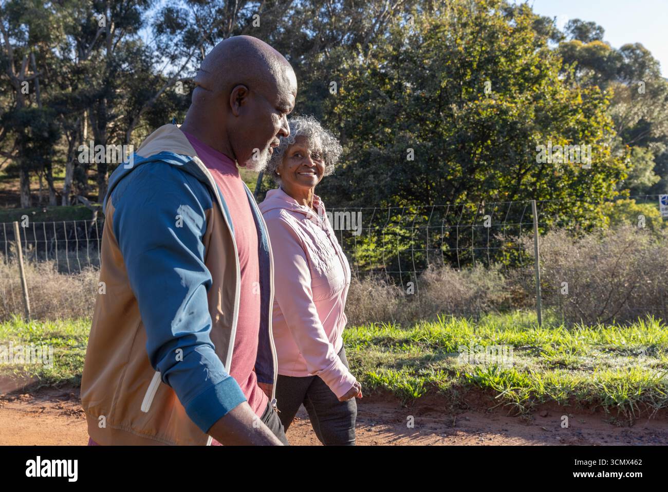 Verschiedene Seniorenpaare spazieren und plaudern entlang des ländlichen Feldwegs, vorbei an Drahtzaun und grünem Gras Stockfoto