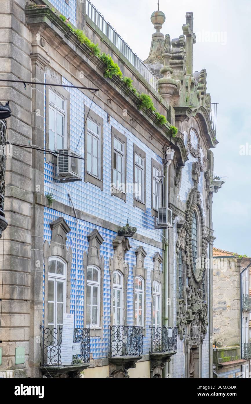 Seitenansicht des historischen Gebäudes in Porto mit blauen Azulejo-Fliesen und verzierten Steinmetzwerken. Eiserne Balkone, Bogenfenster, architektonischer Kontrast, kulturell Stockfoto