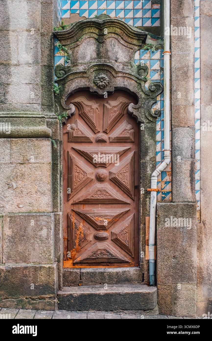 Holztür mit geometrischen Schnitzereien und Schachbrettfliesen in Porto. Steinbogen mit Scrollwerk, blaue Keramikmuster, historisch Stockfoto