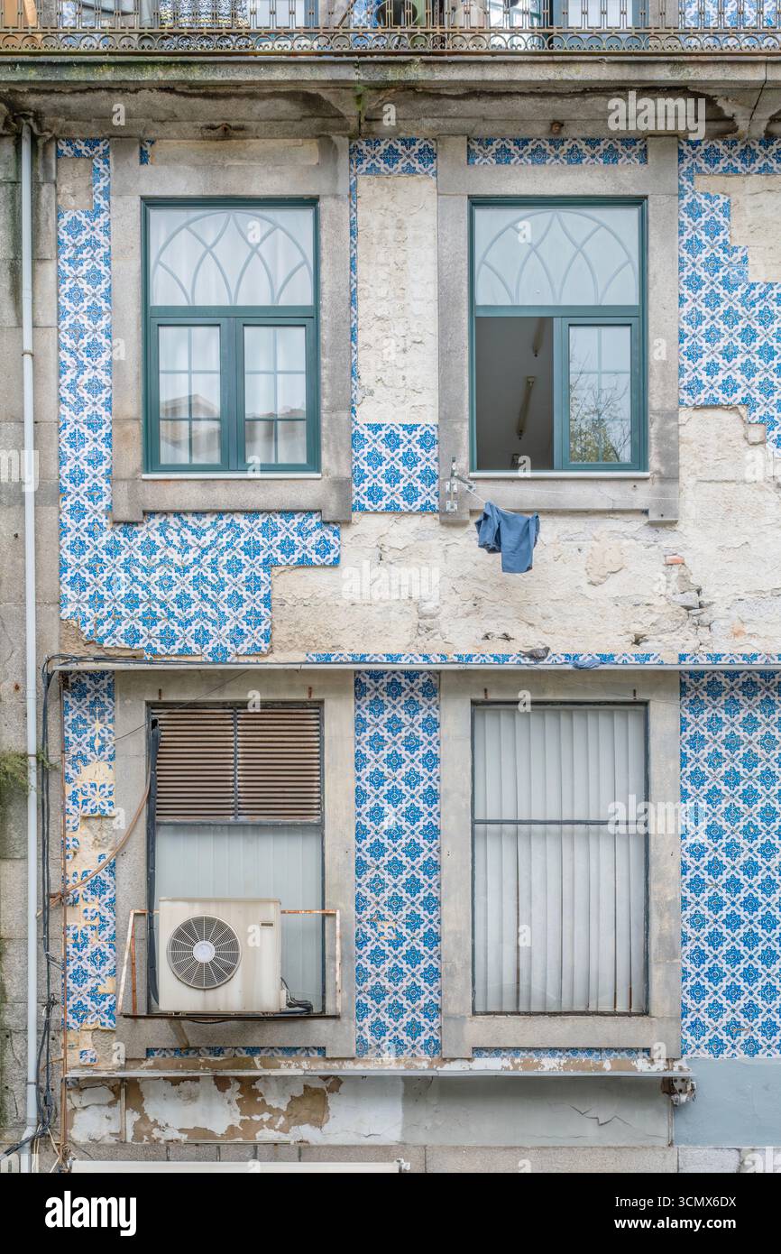 Verwitterte Gebäudefassade mit gewölbten und rechteckigen Fenstern und abgenutzten Azulejo-Fliesen in Porto. Klimaanlage, Hängetuch, urbaner Verfall Stockfoto