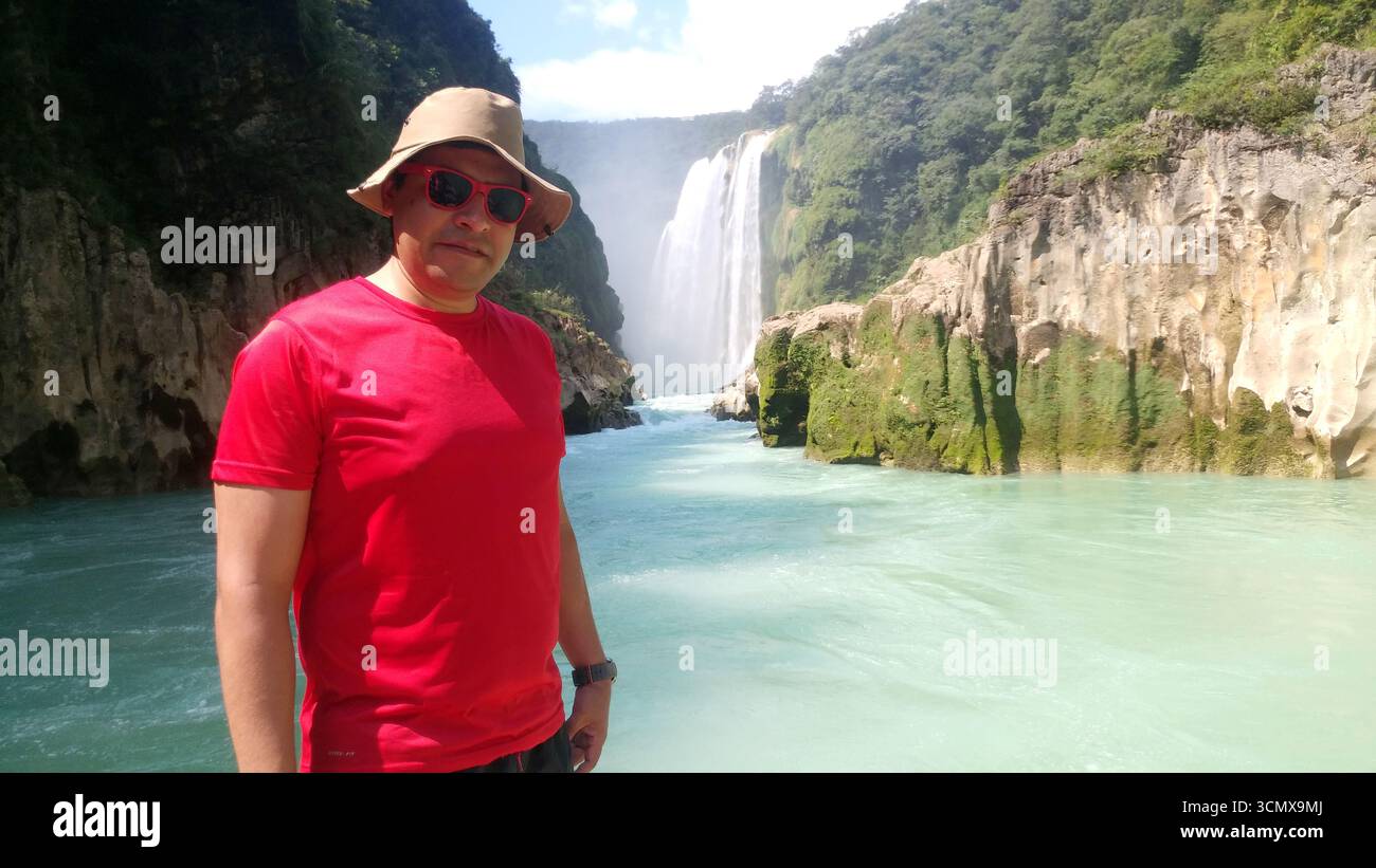 Ein erwachsener Latino-Mann mit Hut, Hemd und roter Brille besucht den Pier des Tamul-Wasserfalls in Huasteca Potosina als Erholung und Entspannung im Urlaub Stockfoto