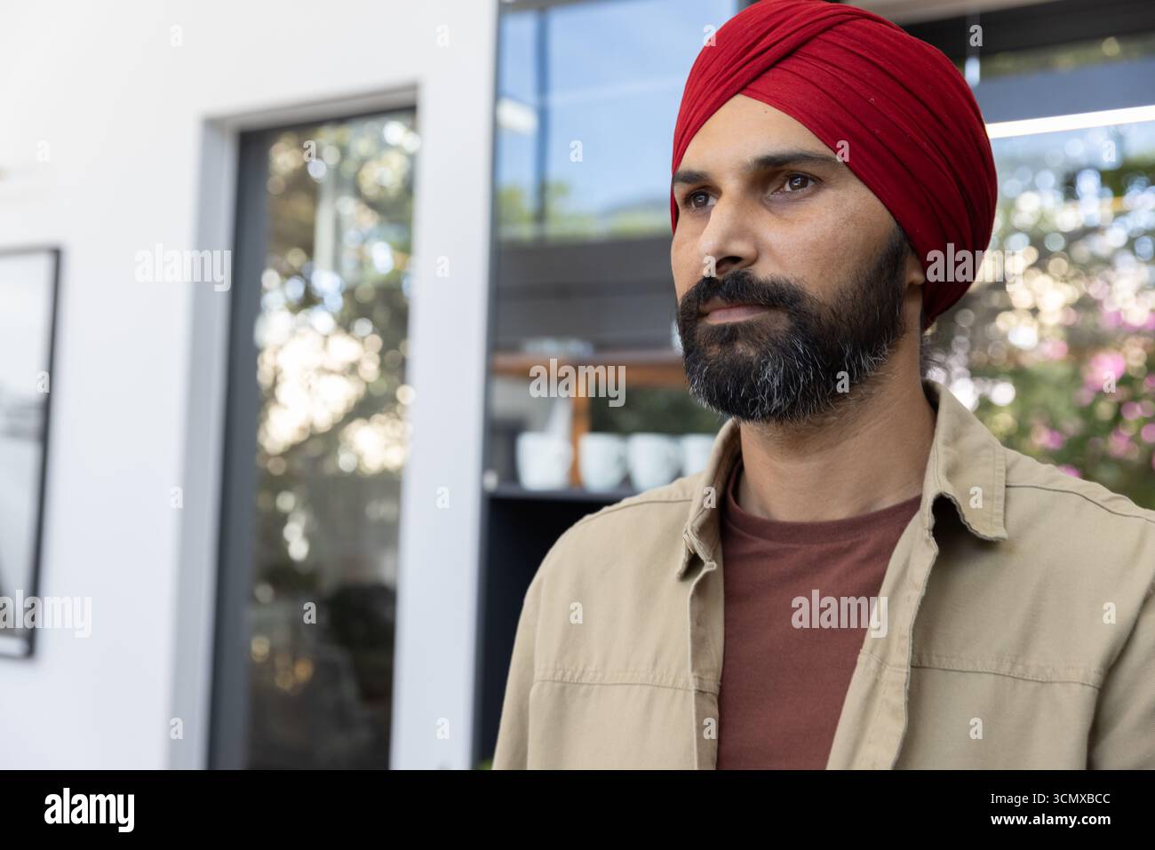 Indischer Mann mit rotem Turban, der an Regalen steht und Becher in der modernen Küche hält, Kopierraum Stockfoto