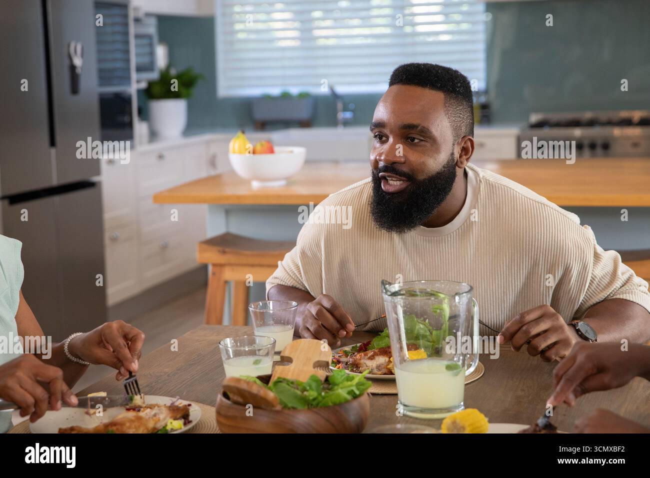 Afroamerikanische Familie sitzt am Tisch in der Küche und isst Hühnchensalat und gießt einen Drink aus dem Pitcher Stockfoto