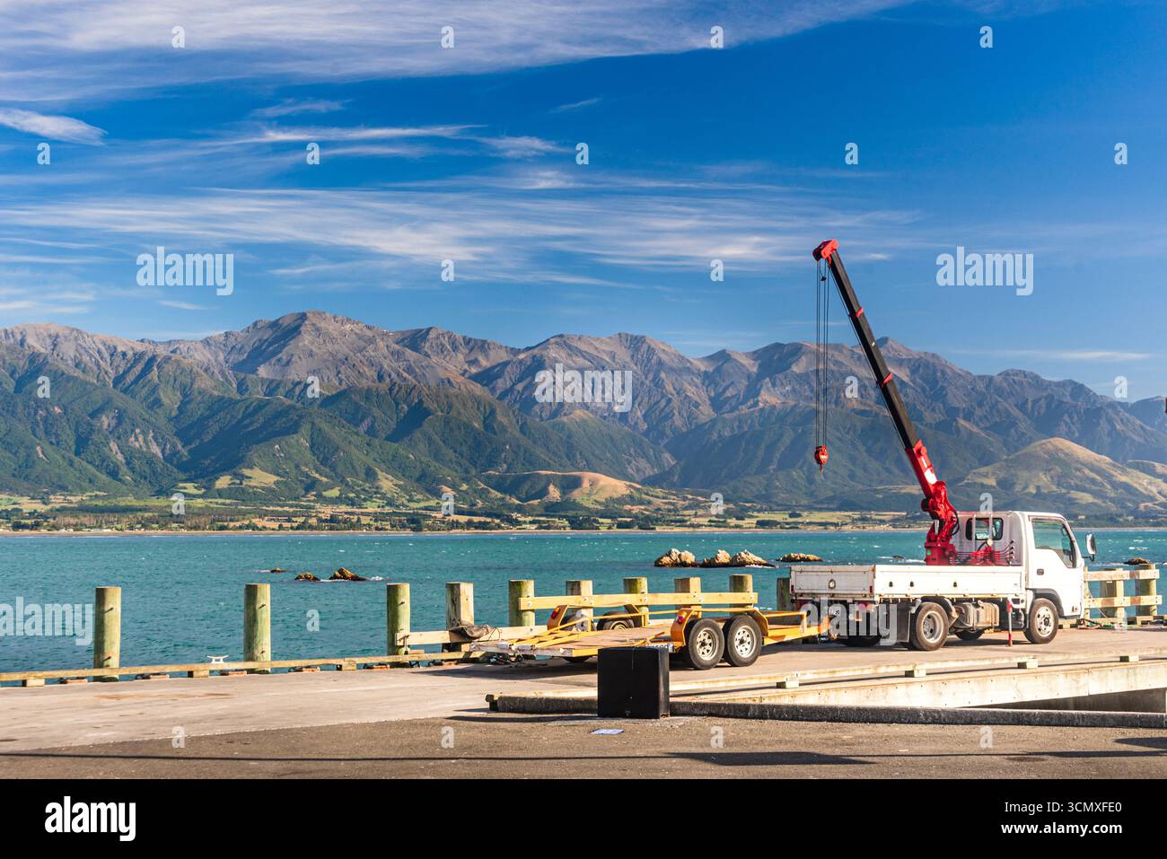 Red Crane Truck auf Sunny Wharf mit Coastal Mountains und Calm Sea im South Bay Harbour, Kaikoura Peninsula, Neuseeland Stockfoto