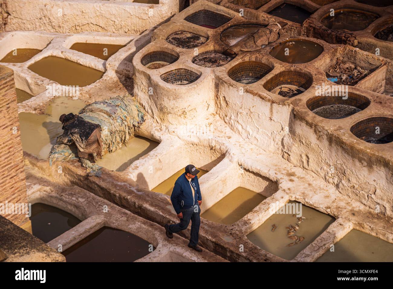 Man läuft entlang der Edge of Dye Gruben in der Chouara Tannery mit weiß getünchten Wänden in Fes, Marokko Stockfoto