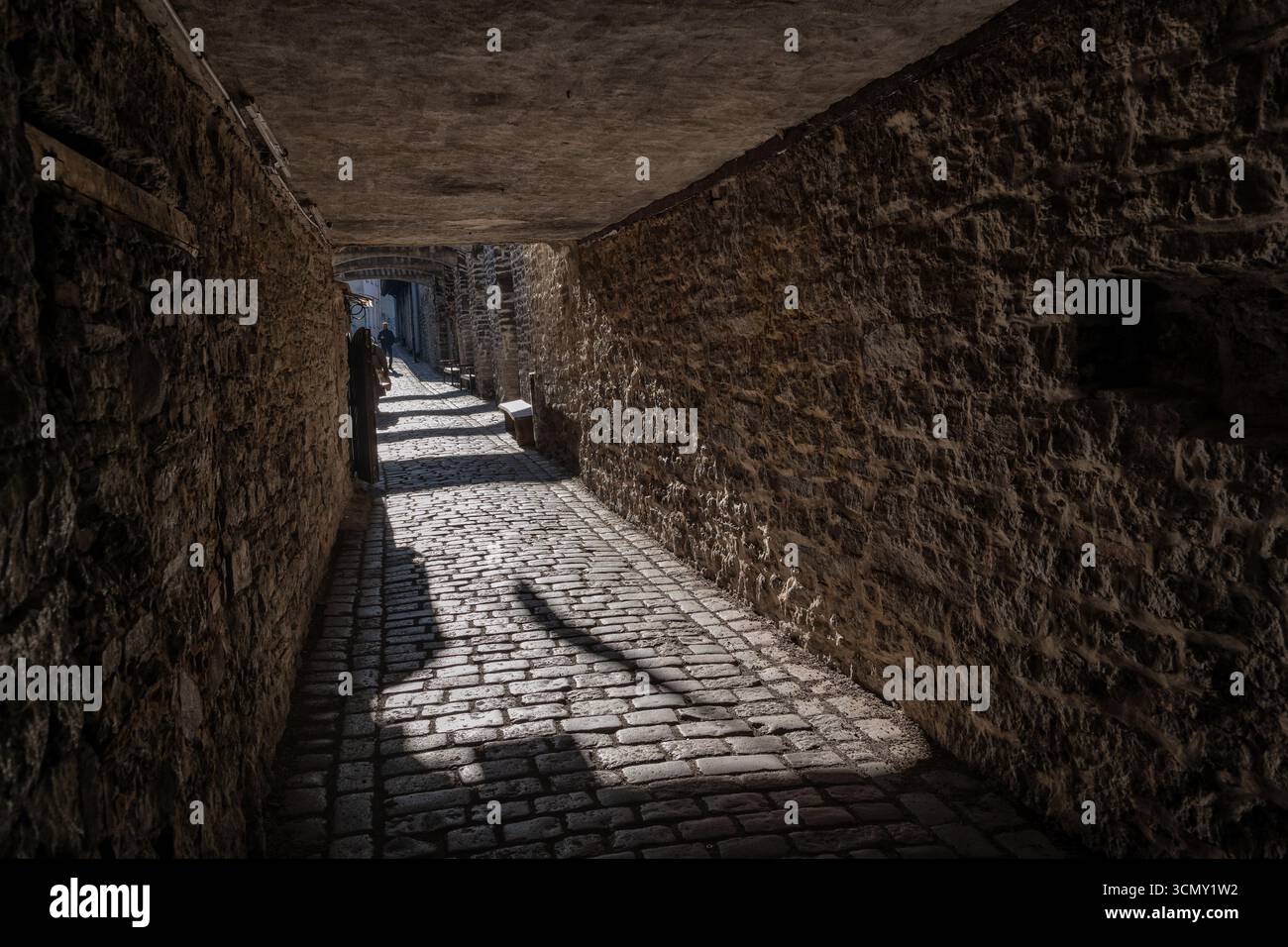Sonnendurchfluteter Durchgang unter dem Gebäude mit schmaler Kopfsteinpflasterstraße, Steinmauern und niedriger Decke in der mittelalterlichen Altstadt in Tallinn, Estland. Stockfoto