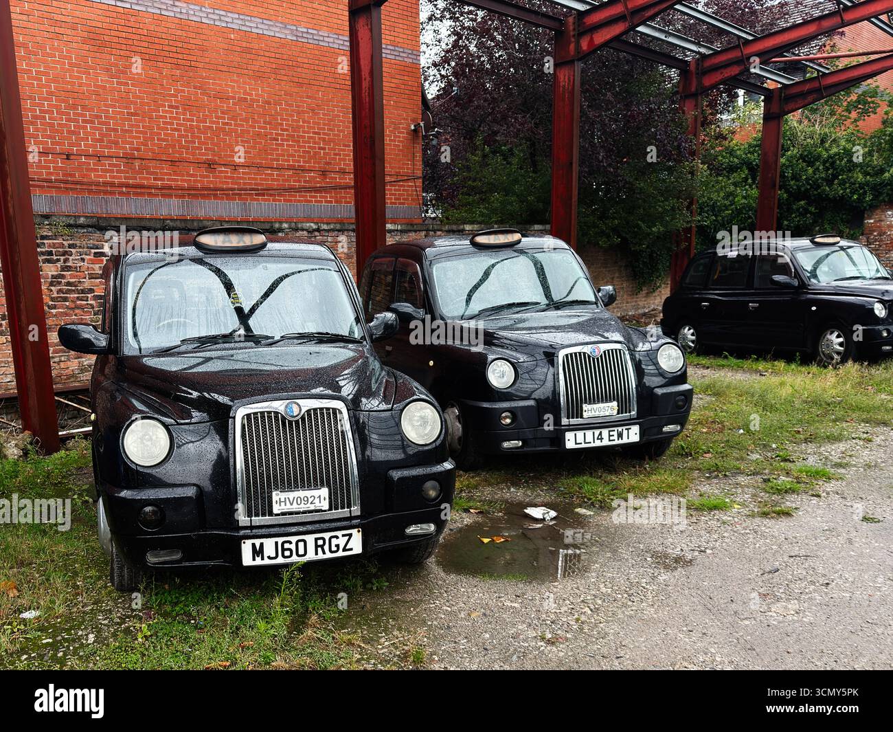 Manchester, Großbritannien - 16. September 2025: Schwarze Taxis im klassischen Londoner Design parkten an einem nassen Tag in Manchester draußen. Stockfoto