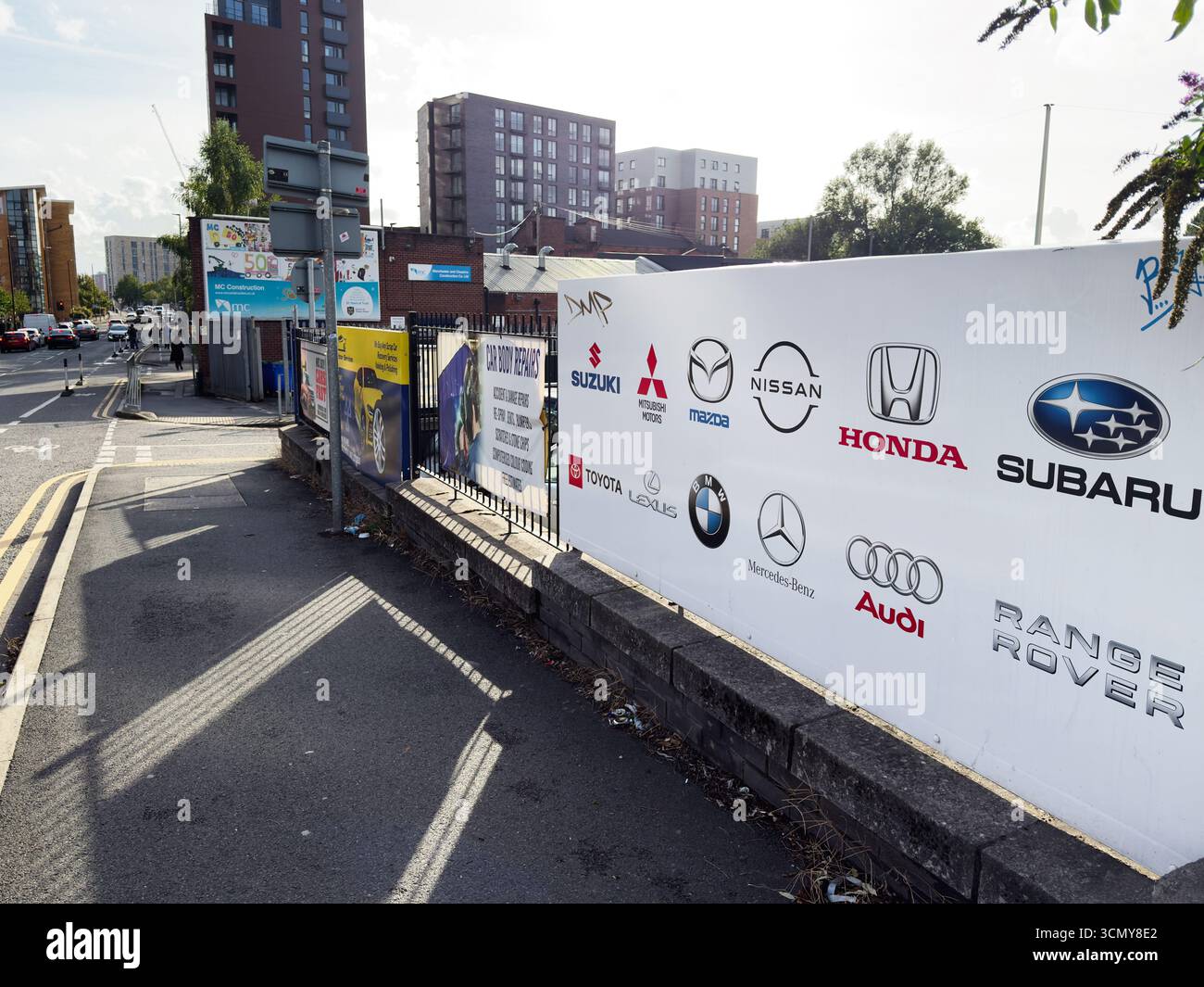 Salford, Großbritannien – 16. September 2025: Salford Street-Szene mit Autologos, städtischen Gebäuden und Werbung entlang eines Gehwegs. Stockfoto
