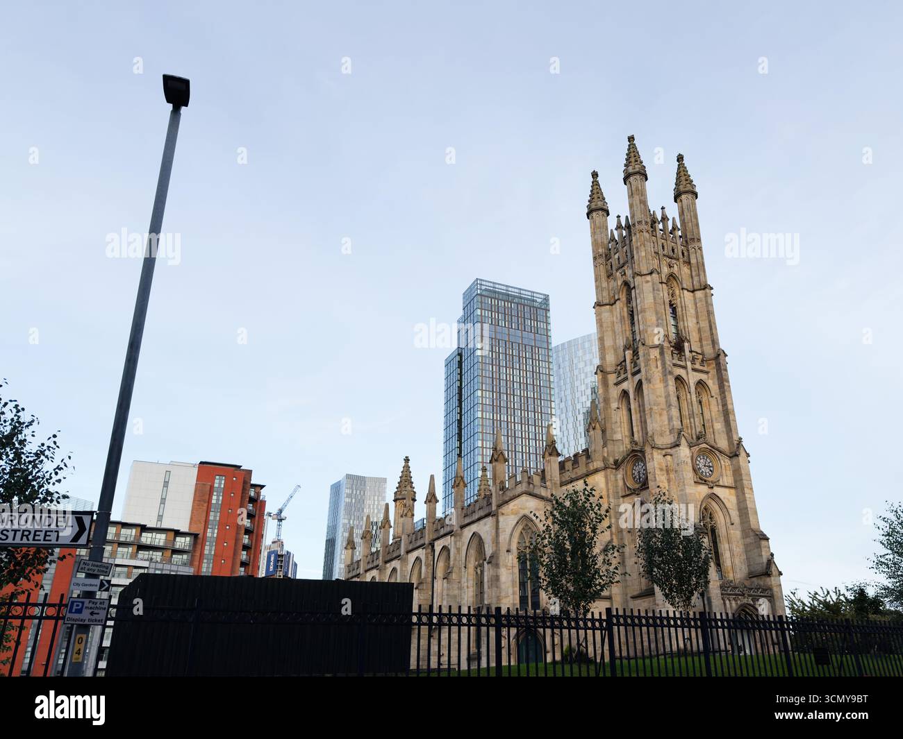 Manchester, Großbritannien - 16. September 2025: Kontrast zwischen der historischen Kirche St. George, Chester Road, Hulme-Architektur und modernen Wolkenkratzern in Manchester, Stockfoto