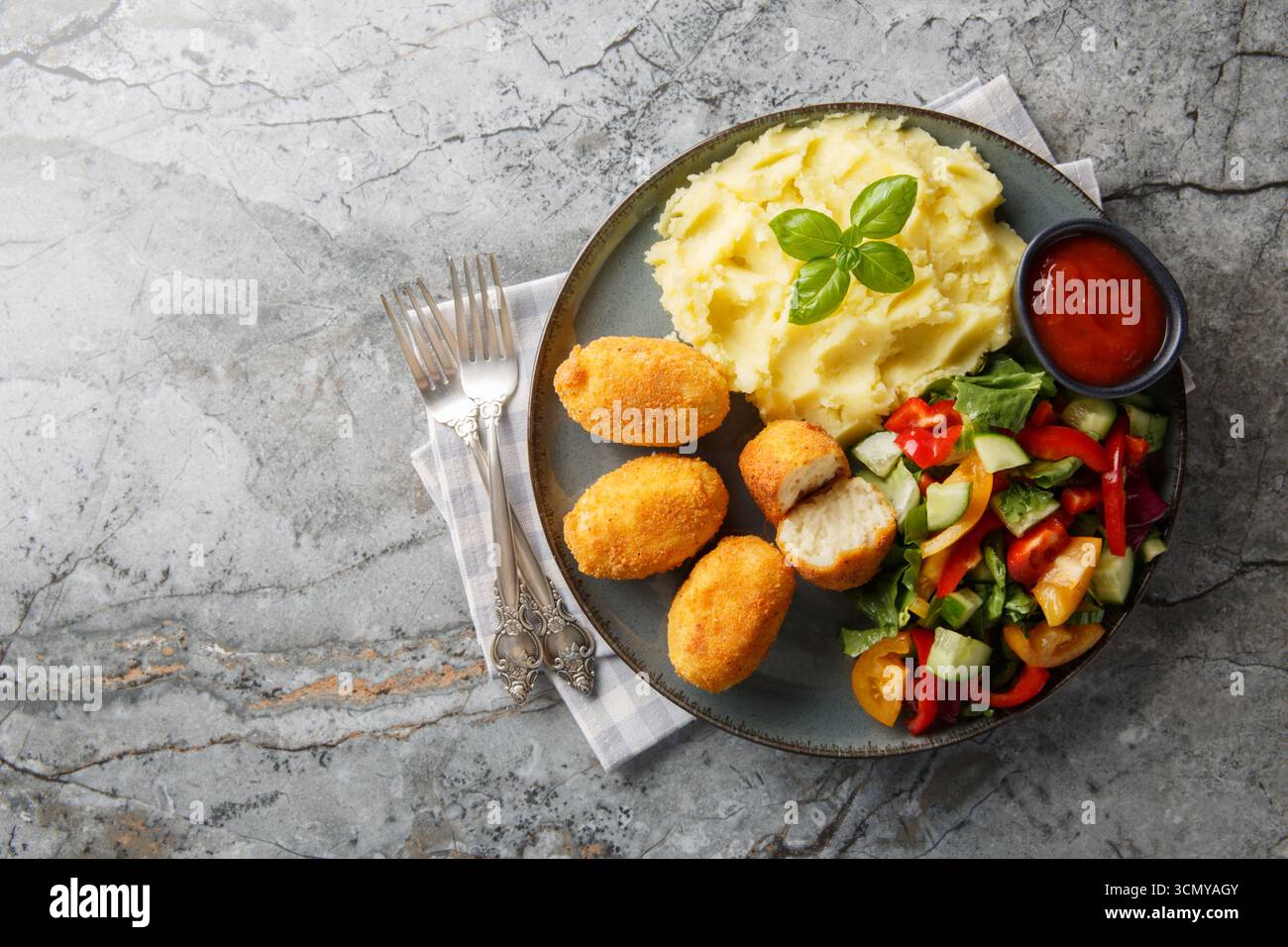 Heiße Hähnchenbechamelkroketten mit Kartoffelpüree, Gemüsesalat und Ketchup in Nahaufnahme auf einem Teller auf dem Tisch. Horizontale Draufsicht von oben Stockfoto