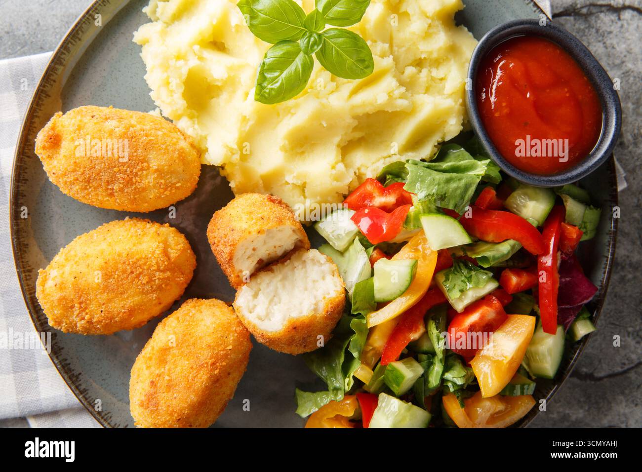 Panierte und frittierte Hähnchenkroketten, serviert mit Kartoffelpüree, frischem Salat und Tomatensauce in Nahaufnahme auf einem Teller auf dem Tisch. Horizontale Draufsicht f Stockfoto