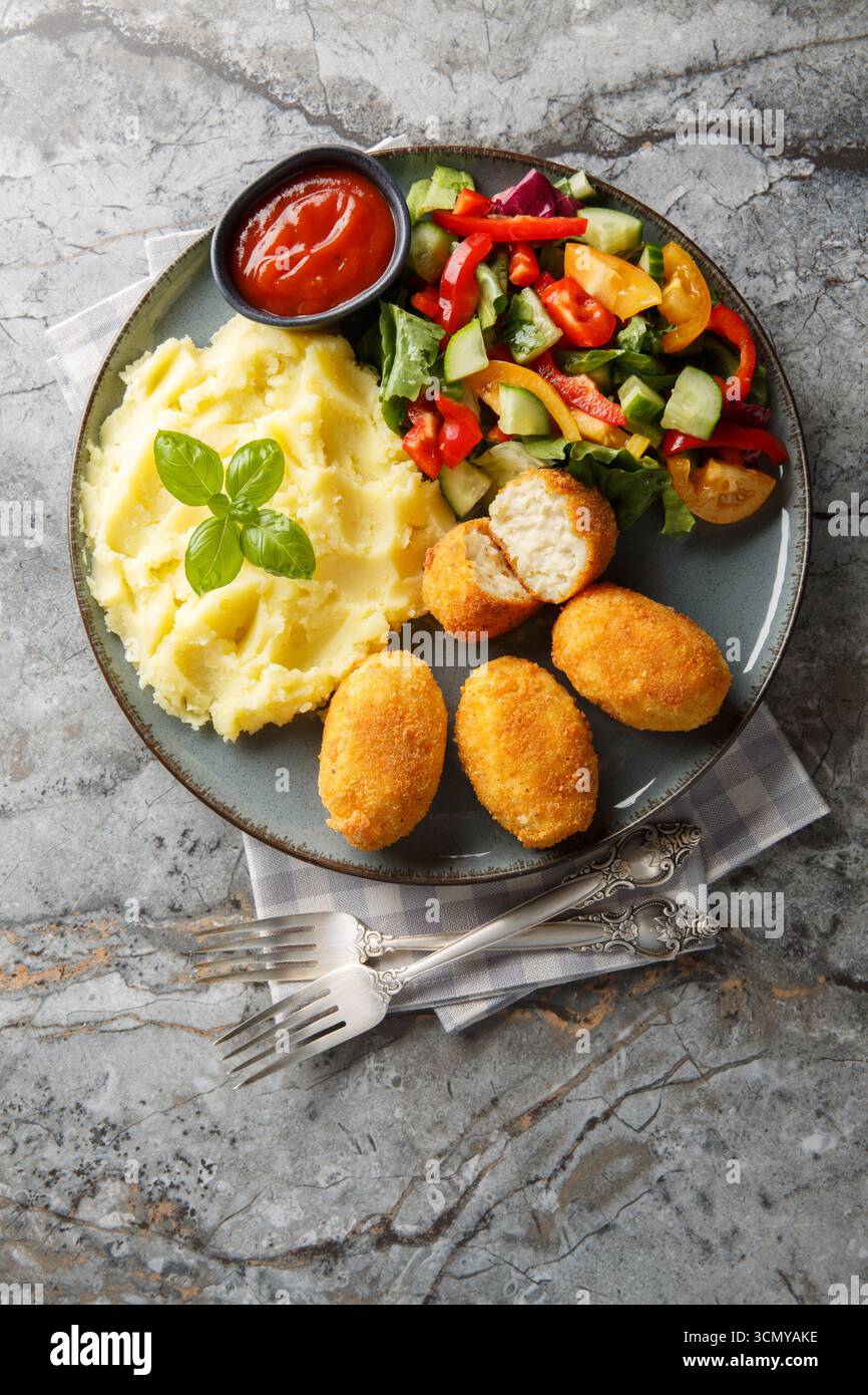 Nahaufnahme von spanischen Hähnchenkroketten mit Kartoffelpüree, Gemüsesalat und Ketchup auf einem Teller auf einem Tisch. Vertikale Draufsicht von oben Stockfoto