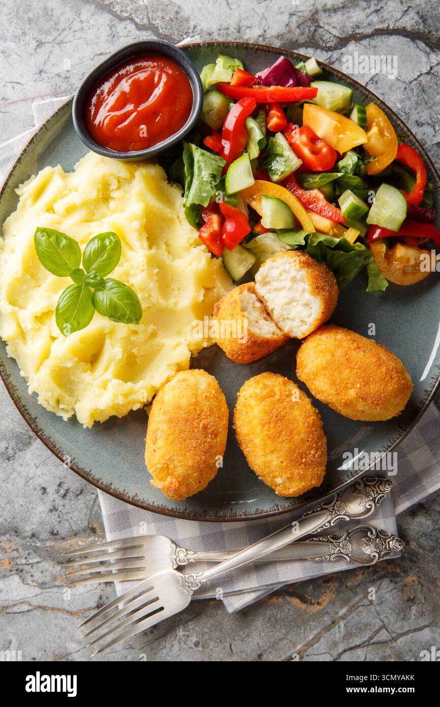 Hähnchenkroketten Croquetas de Pollo mit Kartoffelpüree, Gemüsesalat und Ketchup in Nahaufnahme auf einem Teller auf dem Tisch. Vertikale Draufsicht von oben Stockfoto