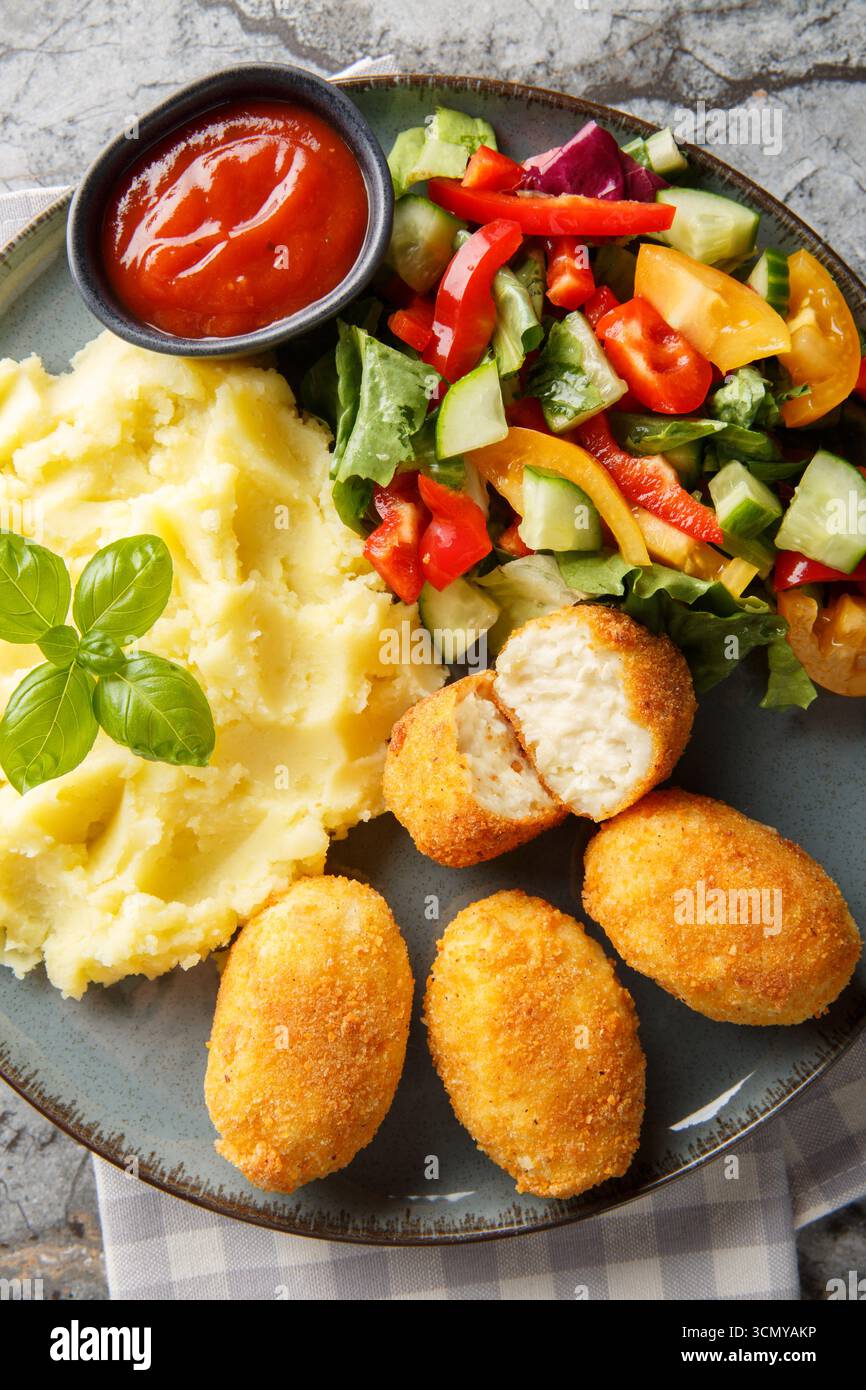 Köstliche knusprige panierte Hähnchenkroketten serviert mit Kartoffeln, frischem Salat und Tomatensauce in Nahaufnahme auf einem Teller auf dem Tisch. Vertikal oben VI Stockfoto