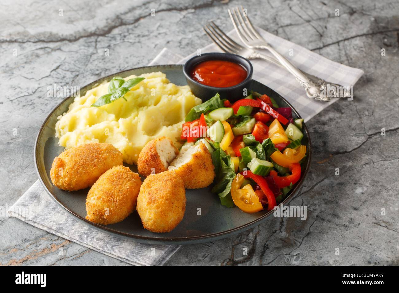 Heiße Hähnchenbechamelkroketten mit Kartoffelpüree, Gemüsesalat und Ketchup in Nahaufnahme auf einem Teller auf dem Tisch. Horizontal Stockfoto