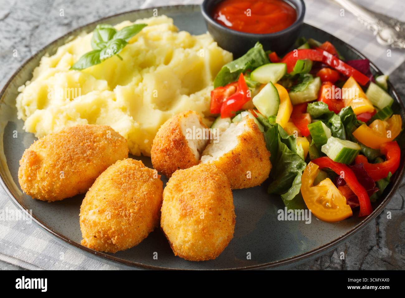 Panierte und frittierte Hähnchenkroketten, serviert mit Kartoffelpüree, frischem Salat und Tomatensauce in Nahaufnahme auf einem Teller auf dem Tisch. Horizontal Stockfoto