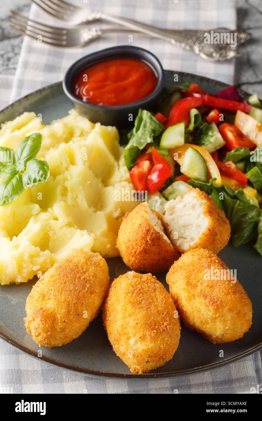Hähnchenkroketten Croquetas de Pollo mit Kartoffelpüree, Gemüsesalat und Ketchup in Nahaufnahme auf einem Teller auf dem Tisch. Vertikal Stockfoto