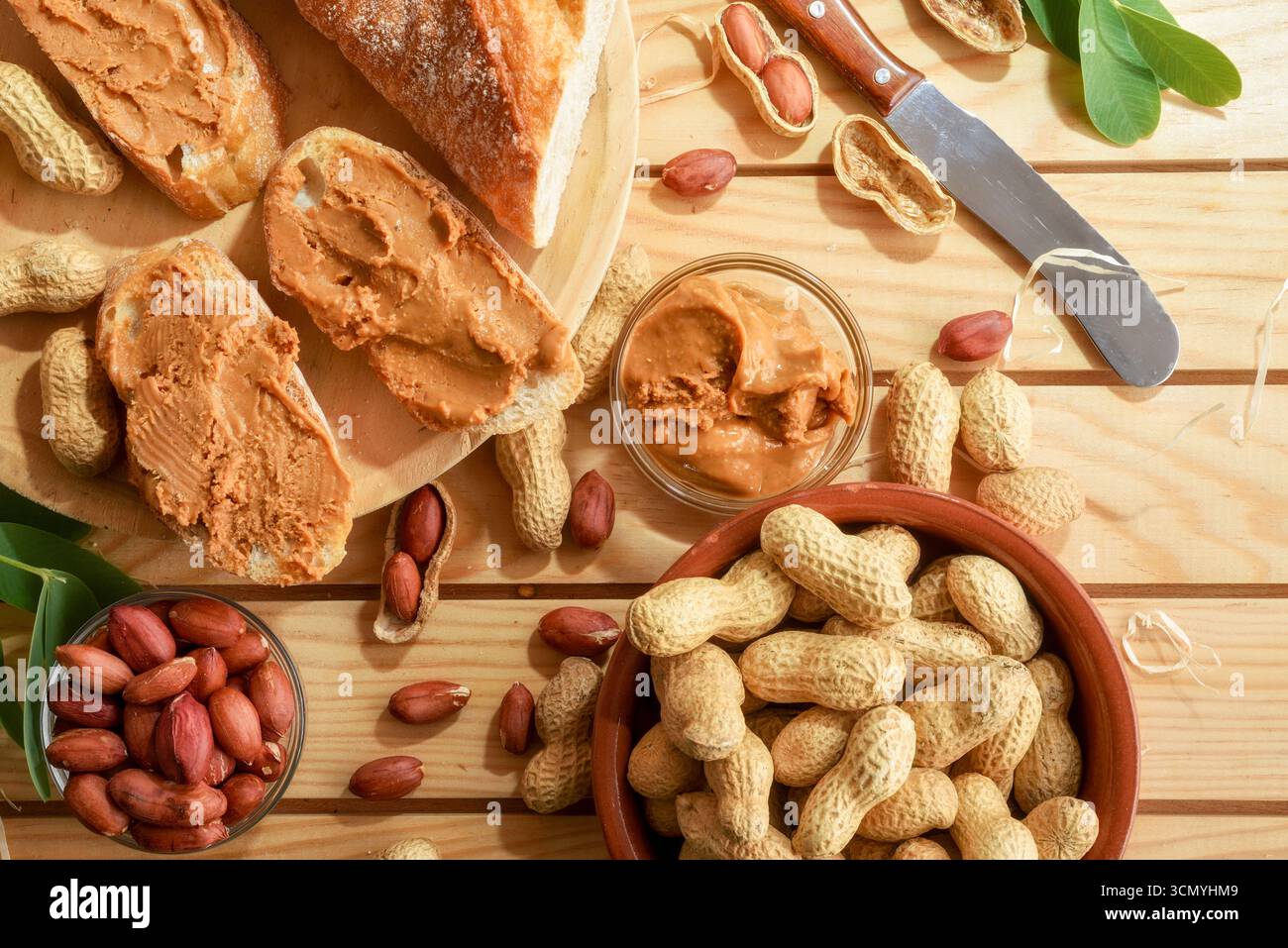 Frisch geerntete hausgemachte Erdnussbutter und Brotscheiben auf einem Holztisch mit Obst draußen in der Sonne. Draufsicht. Stockfoto