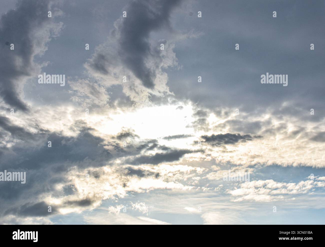 Heller Tageshimmel mit weißen bis dunkelgrauen Wolken, die von Sonnenlicht beleuchtet werden und sanftes natürliches Licht und dezente atmosphärische Töne zeigen. Stockfoto