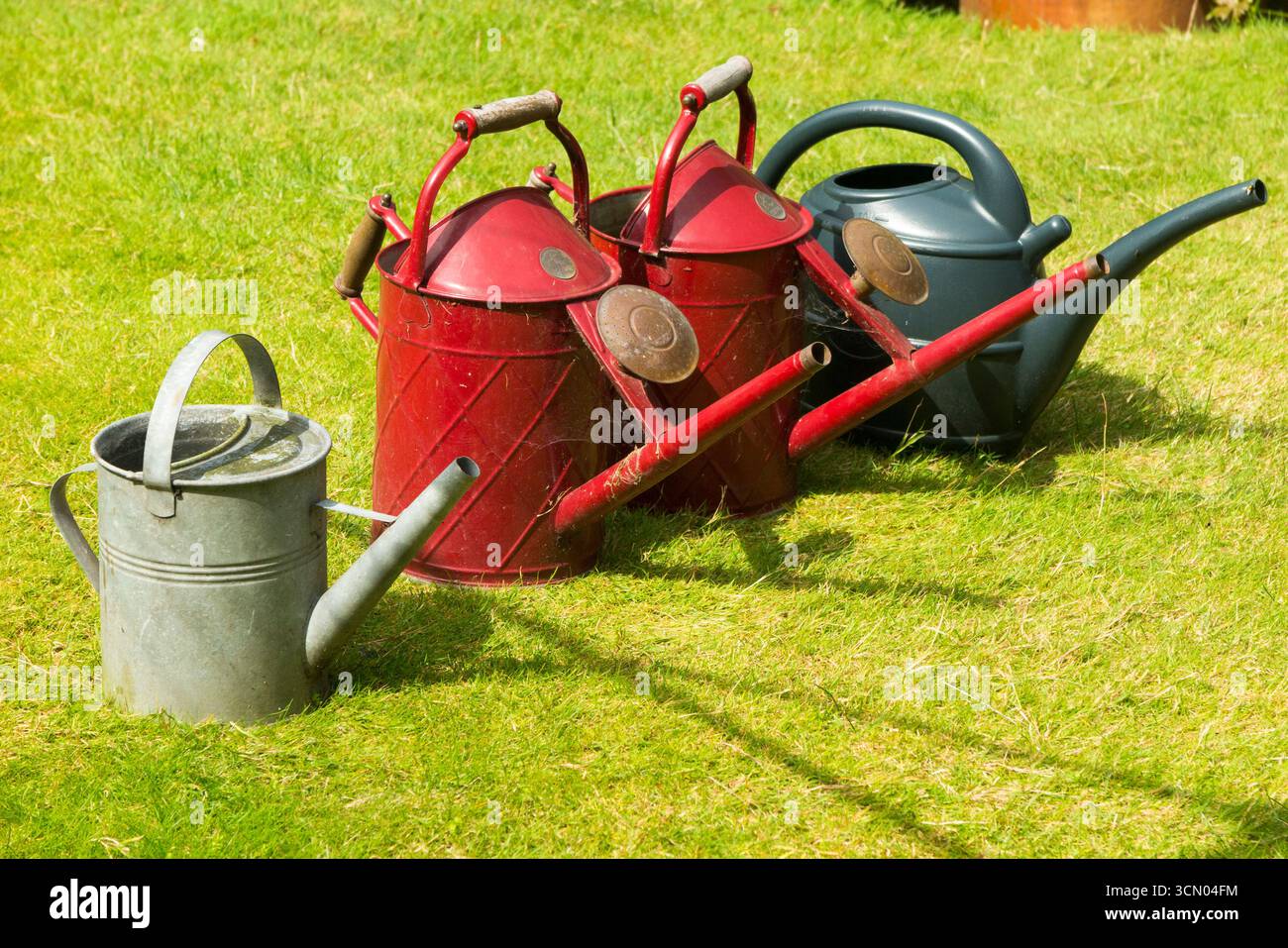 Gießkannen, einige mit Wasser, in einer Linie auf einem grünen Rasen während eines Sommerschlauchrohrverbots in Großbritannien aufgrund von Dürre. (140) Stockfoto