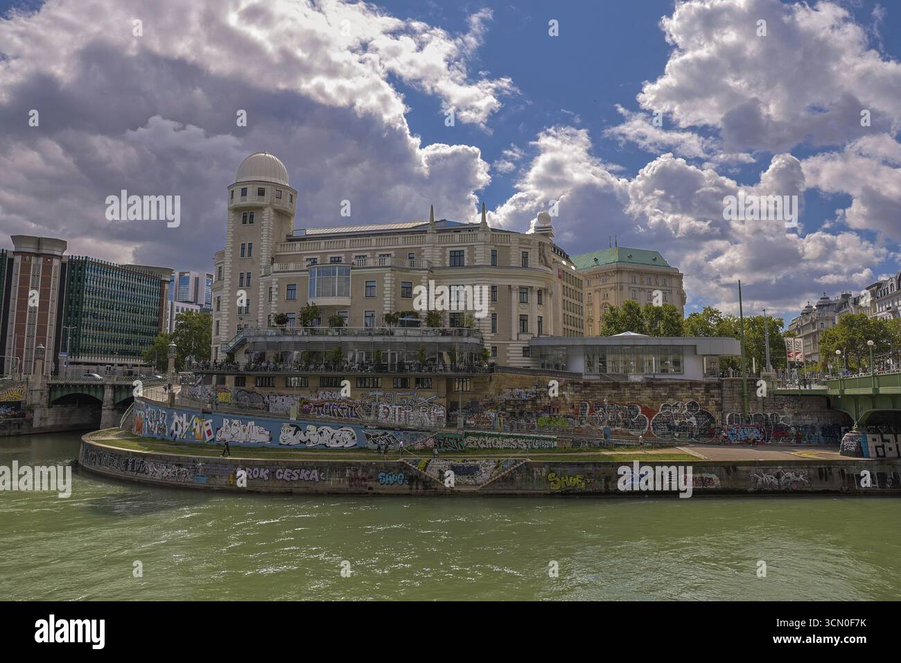 Ein historisches Gebäude am Fluss mit Graffiti, unter klarem Himmel, umgeben von urbaner Umgebung Urania Ringstraße Wien Österreich Stockfoto