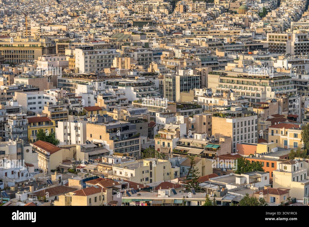 Erhöhter Blick auf dichte mittelhohe Dächer und Terrassen im Zentrum von Athen, mit vielfältigen Gebäudefassaden und Dachgärten im warmen späten Licht, Griechenland. Stockfoto