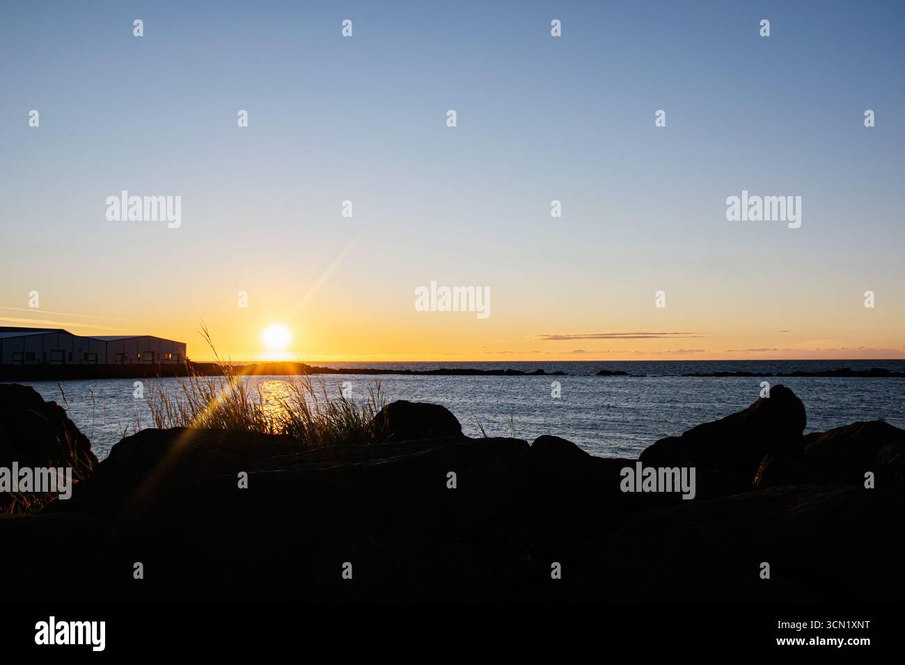 Ruhiger Sonnenaufgang über der isländischen Küste mit einem ruhigen felsigen Vordergrund Stockfoto