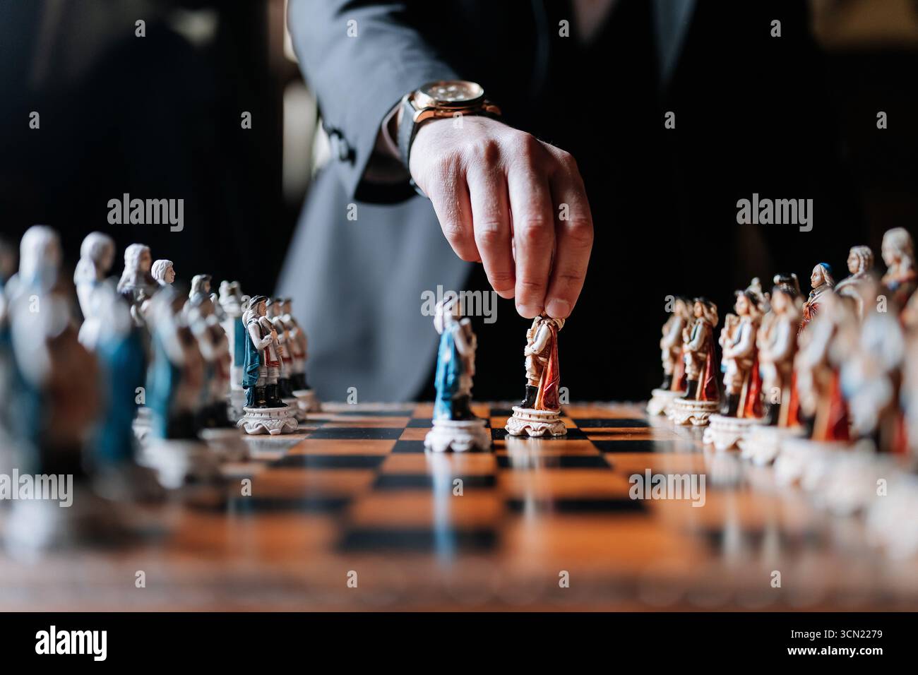 Mann im Anzug, der Schach mit kunstvollen Stücken auf luxuriösem Holzbrett spielt Stockfoto